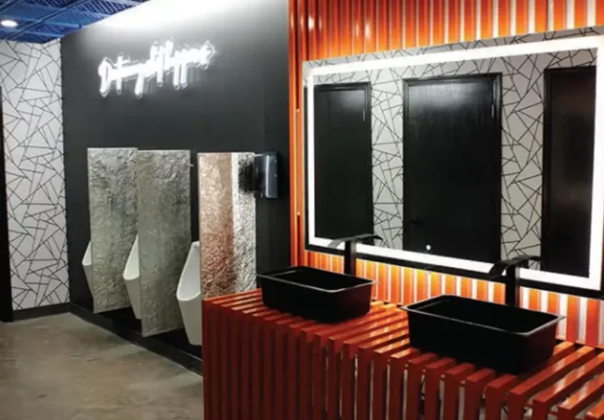 Commercial restroom with an orange timber vanity, black basins, backlit mirrors and a neon sign