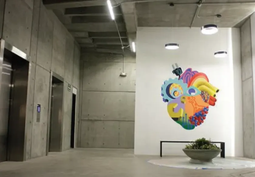 Lobby of the MIND building in Tijuana: exposed concrete, circular and linear light fixtures, a steel bench and a mural